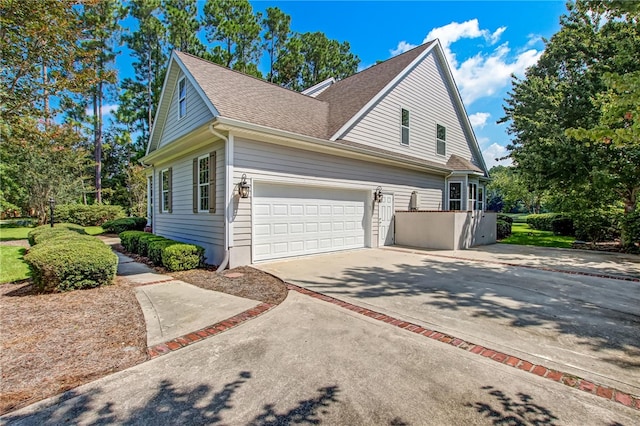 view of side of home with a garage, roof with shingles, and driveway