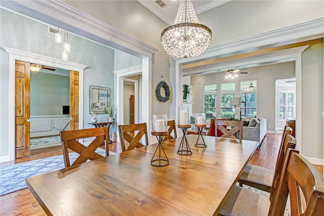 dining area with wood-type flooring, visible vents, crown molding, and ceiling fan with notable chandelier