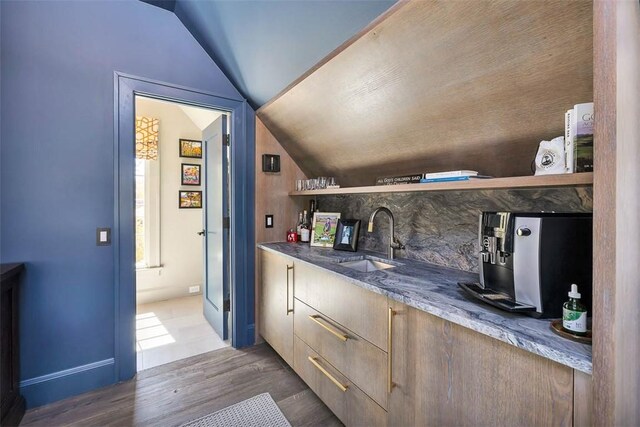 bar with dark hardwood / wood-style flooring, sink, dark stone counters, and lofted ceiling