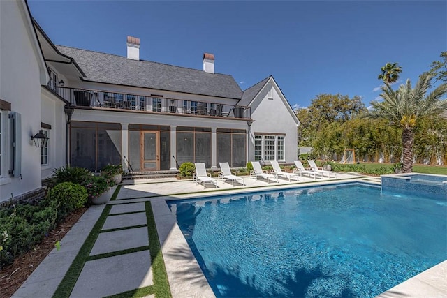 back of property with a swimming pool with hot tub, a balcony, and a patio area