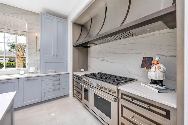 kitchen with wall chimney range hood, gray cabinetry, light tile patterned flooring, and range with two ovens