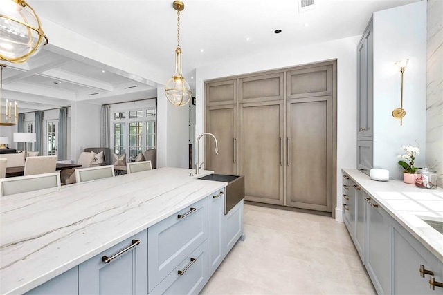 kitchen featuring gray cabinetry, light stone countertops, sink, beamed ceiling, and decorative light fixtures