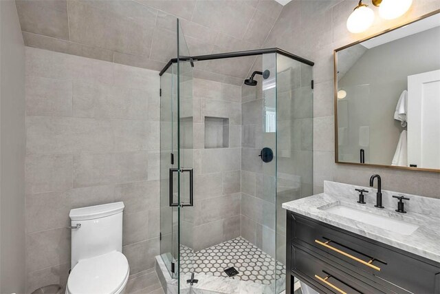 bathroom with vanity, a shower with shower door, tile walls, and toilet