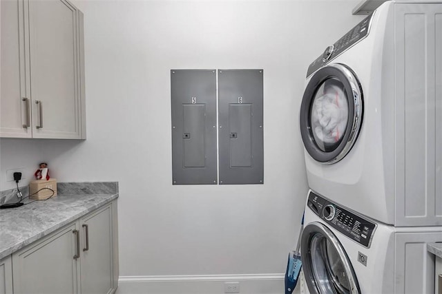 washroom featuring cabinets, electric panel, and stacked washer and clothes dryer