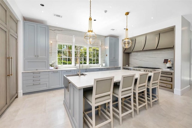 kitchen featuring pendant lighting, a breakfast bar, gray cabinetry, a center island with sink, and tasteful backsplash