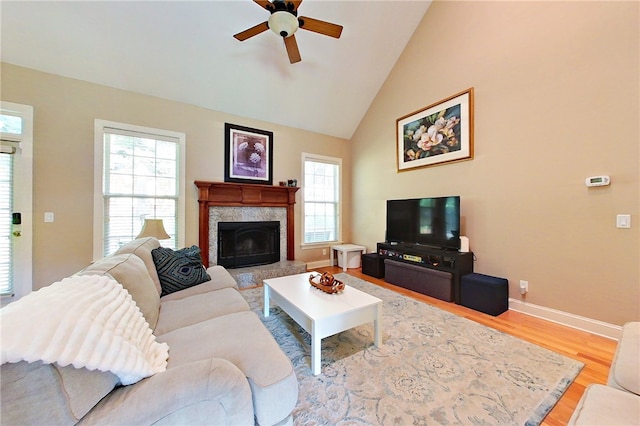 living room with ceiling fan, light hardwood / wood-style flooring, a high end fireplace, and high vaulted ceiling