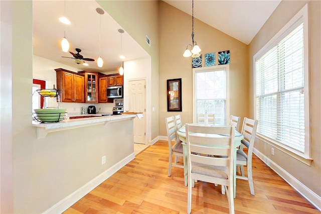 dining room featuring ceiling fan with notable chandelier, light hardwood / wood-style floors, and vaulted ceiling