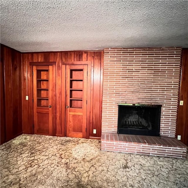 unfurnished living room featuring a textured ceiling, a fireplace, carpet flooring, and wooden walls