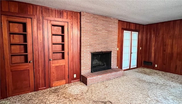 unfurnished living room featuring carpet, a textured ceiling, a brick fireplace, and wooden walls