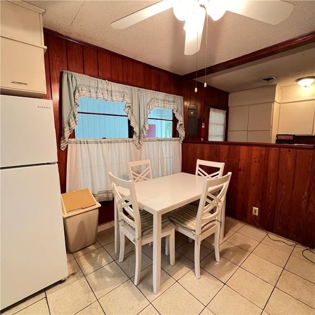 dining area featuring wood walls, light tile patterned floors, visible vents, and a textured ceiling