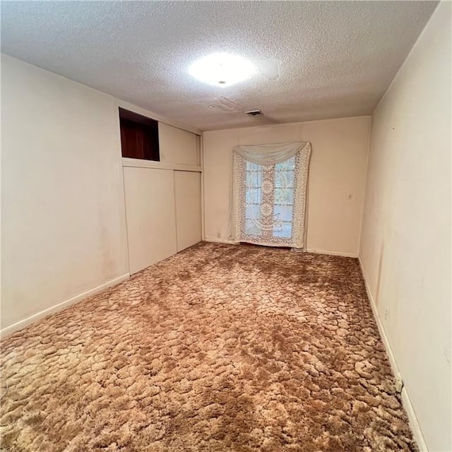 carpeted empty room featuring a textured ceiling, visible vents, and baseboards