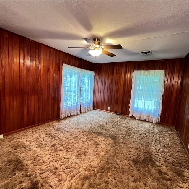 unfurnished room featuring wood walls, ceiling fan, visible vents, and carpet flooring