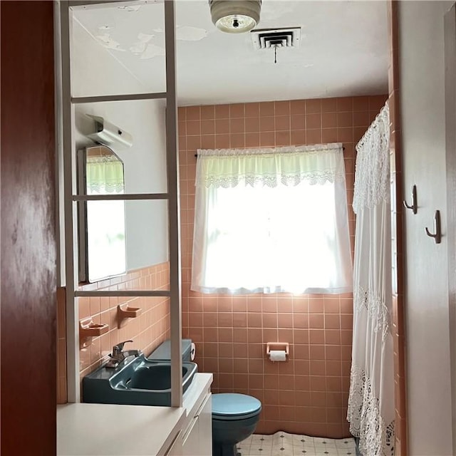 bathroom with toilet, visible vents, vanity, and tile walls