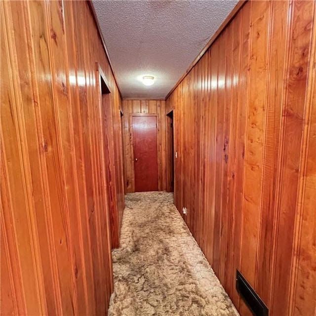 hall featuring a textured ceiling, wooden walls, and carpet flooring