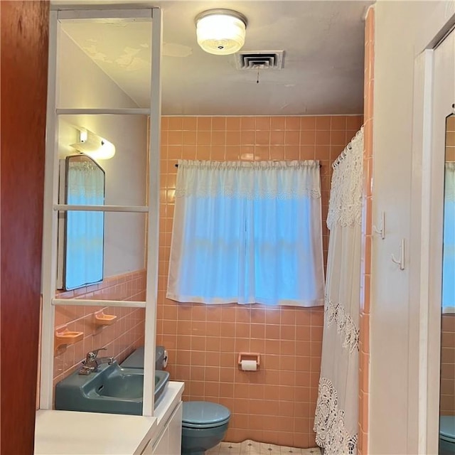 bathroom featuring visible vents, toilet, a shower with curtain, vanity, and tile walls