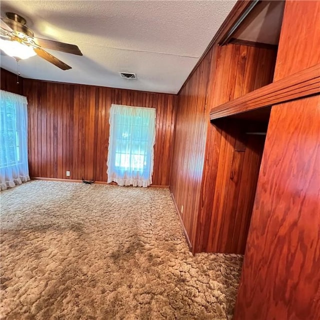 carpeted spare room featuring visible vents, ceiling fan, wooden walls, and a textured ceiling