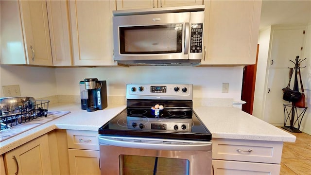 kitchen with cream cabinets, light tile patterned flooring, and stainless steel appliances