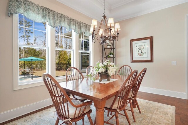 dining space featuring wood finished floors, ornamental molding, a raised ceiling, and baseboards