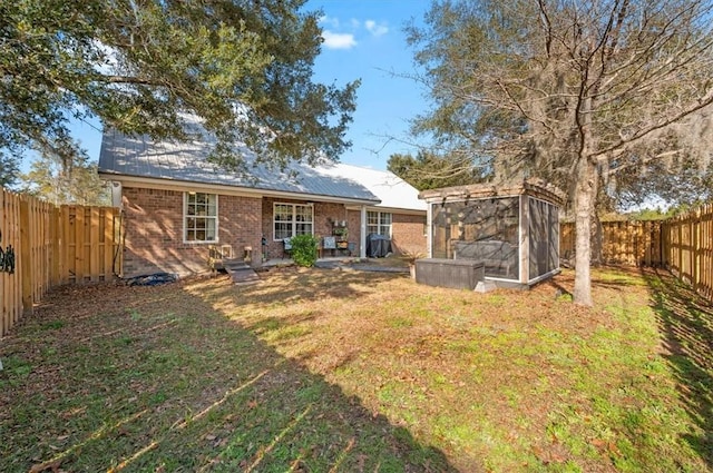 rear view of property with a sunroom, a fenced backyard, a yard, and brick siding