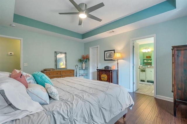 bedroom featuring baseboards, visible vents, a tray ceiling, and wood finished floors