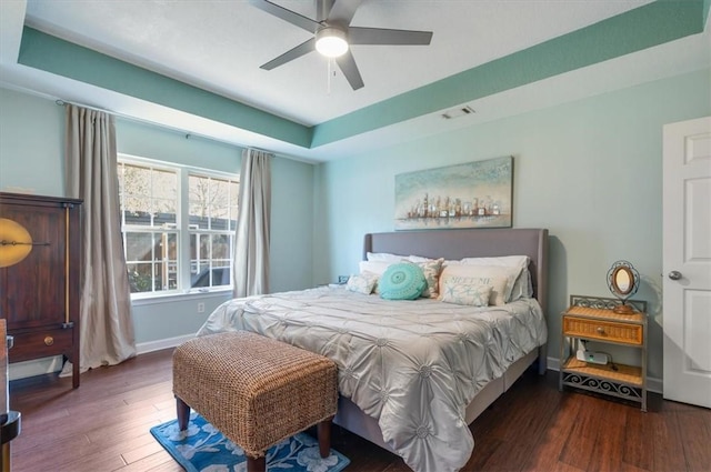 bedroom with ceiling fan, dark wood-type flooring, visible vents, baseboards, and a raised ceiling