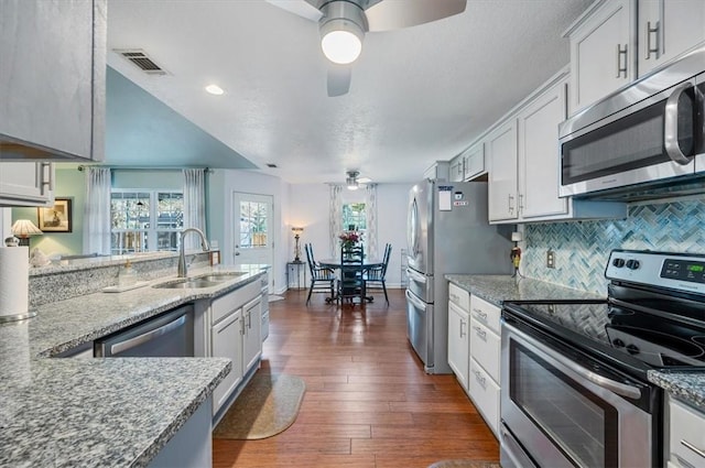 kitchen featuring dark wood-style floors, stainless steel appliances, a sink, ceiling fan, and light stone countertops