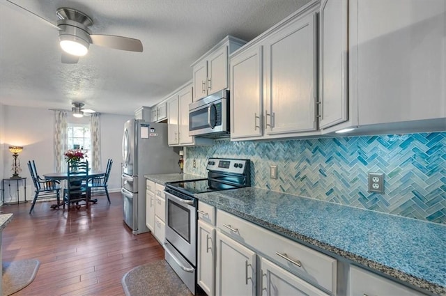 kitchen with appliances with stainless steel finishes, dark wood-type flooring, backsplash, and light stone countertops