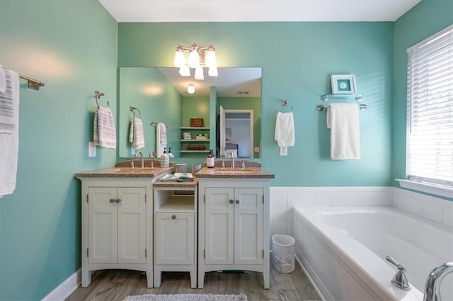 bathroom with a garden tub, double vanity, wood finished floors, and a sink