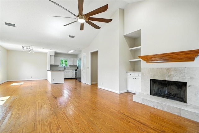 310 Peachtree St, Saint Simons Island, GA 31522 - unfurnished living room with a ceiling fan, a tiled fireplace, built in features, light wood-type flooring, and high vaulted ceiling