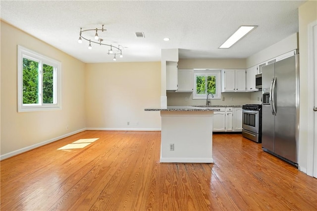 310 Peachtree St, Saint Simons Island, GA 31522 - kitchen featuring stainless steel appliances, white cabinets, light wood-style flooring, a peninsula, and open floor plan