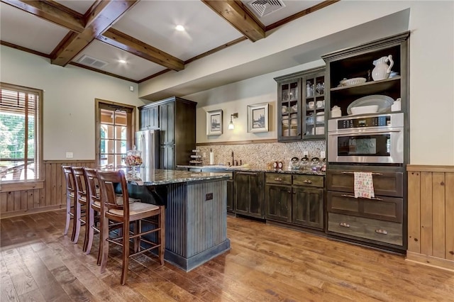 kitchen featuring a breakfast bar, a center island, dark stone counters, beamed ceiling, and stainless steel appliances