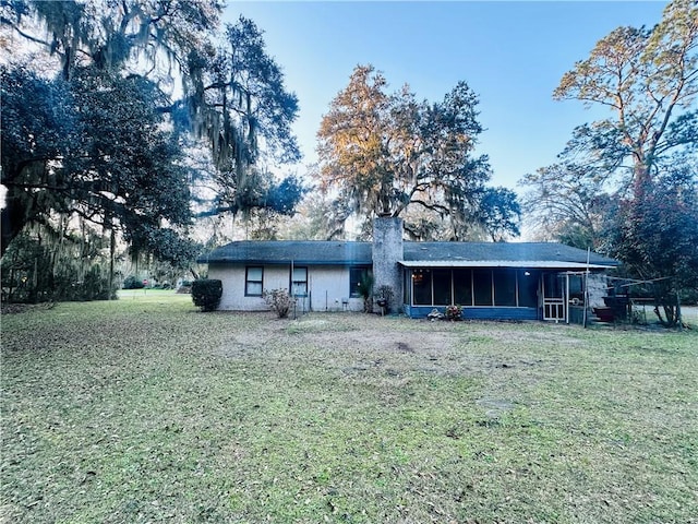 back of property featuring a lawn, a sunroom, and a chimney