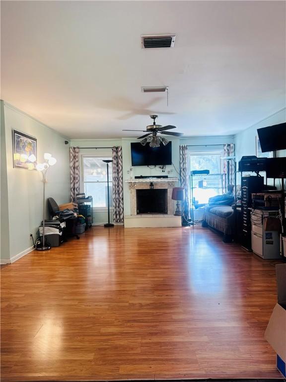 living area featuring a ceiling fan, wood finished floors, a fireplace with raised hearth, and visible vents