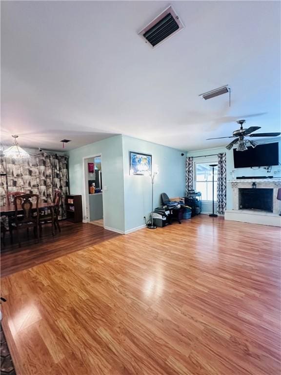 unfurnished living room featuring wood finished floors, baseboards, visible vents, a fireplace with raised hearth, and ceiling fan