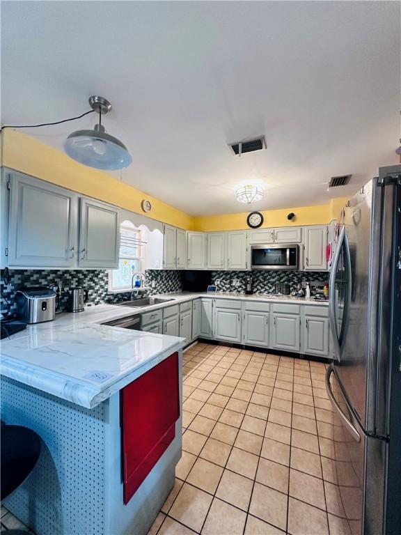 kitchen with visible vents, a sink, stainless steel appliances, a peninsula, and light tile patterned floors