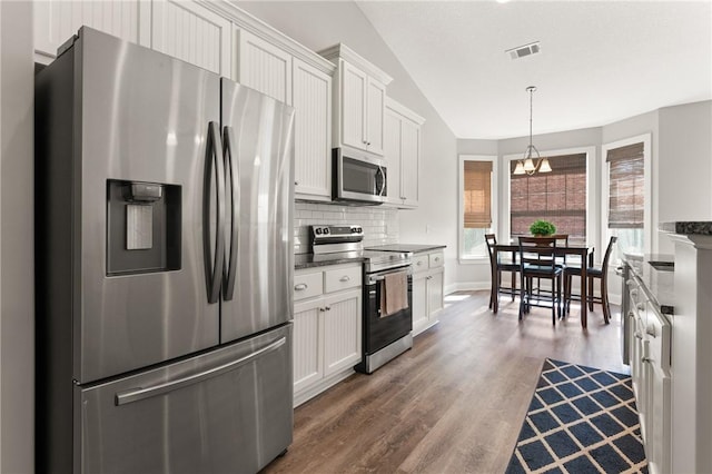 kitchen featuring backsplash, vaulted ceiling, stainless steel appliances, wood finished floors, and white cabinetry