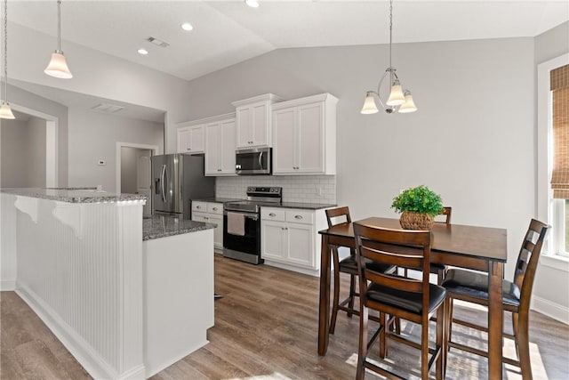 kitchen with wood finished floors, lofted ceiling, stainless steel appliances, white cabinetry, and backsplash