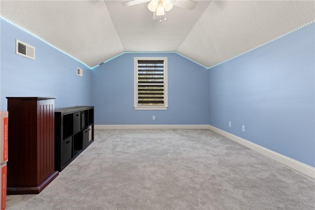 additional living space featuring visible vents, lofted ceiling, light colored carpet, and a textured ceiling