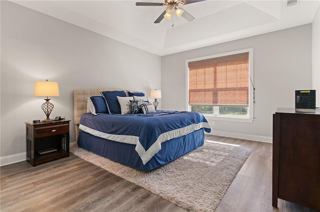 bedroom featuring visible vents, a tray ceiling, baseboards, and wood finished floors