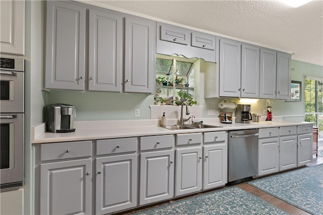 kitchen with gray cabinetry, sink, a textured ceiling, dark hardwood / wood-style flooring, and stainless steel appliances