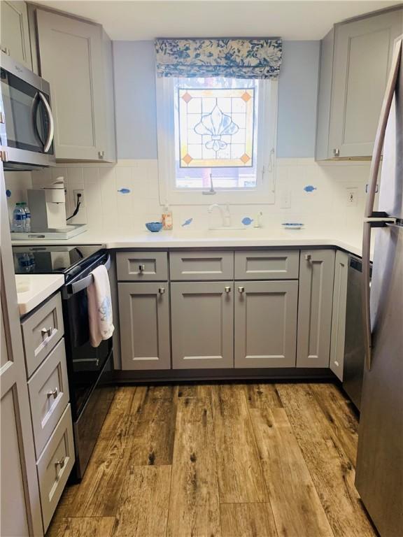 kitchen featuring wood finished floors, gray cabinetry, decorative backsplash, light countertops, and appliances with stainless steel finishes