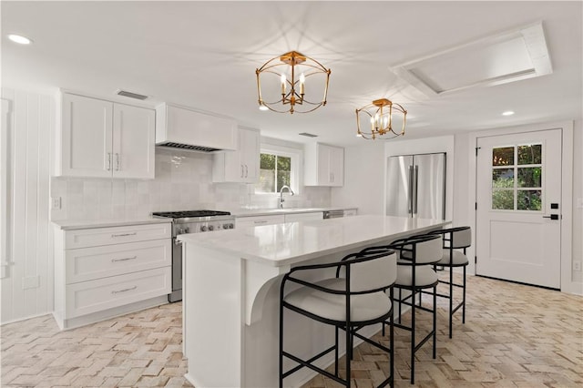 kitchen featuring white cabinets, a kitchen island, stainless steel appliances, decorative backsplash, and hanging light fixtures