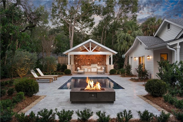 pool at dusk with an outbuilding, an outdoor fire pit, exterior kitchen, and a patio area