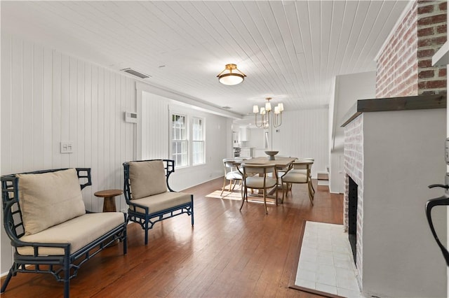 sitting room featuring a brick fireplace, a notable chandelier, wood walls, hardwood / wood-style floors, and wooden ceiling