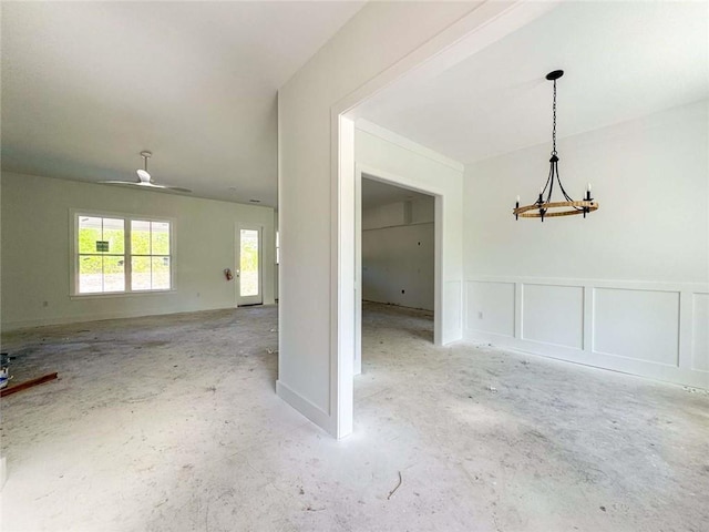 unfurnished room featuring a decorative wall, ceiling fan with notable chandelier, concrete flooring, and a wainscoted wall