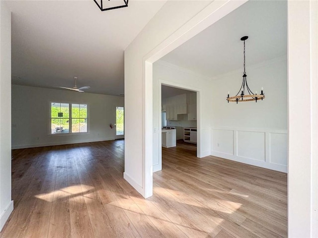 1047 Tranquility Pl NE, Townsend, GA 31331 - unfurnished living room featuring a chandelier, light wood-style flooring, crown molding, a wainscoted wall, and a decorative wall