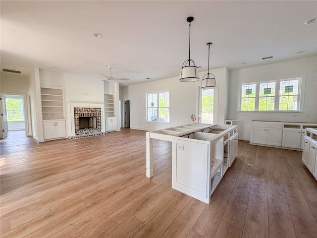 1047 Tranquility Pl NE, Townsend, GA 31331 - kitchen featuring light wood-style floors, ceiling fan, white cabinetry, open shelves, and a fireplace
