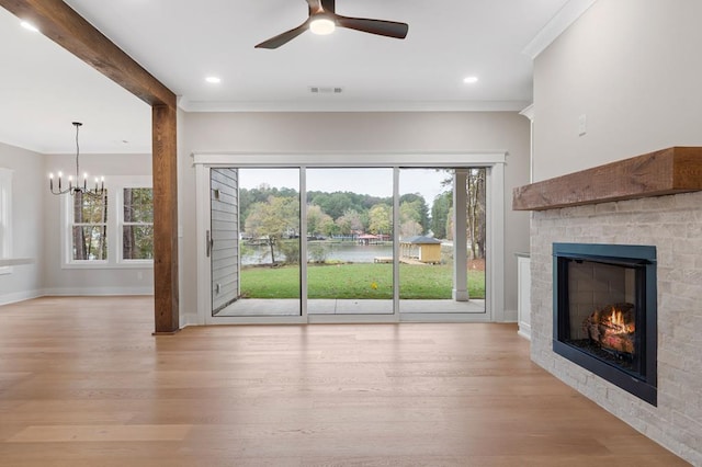 unfurnished living room featuring beamed ceiling, light wood-type flooring, a tiled fireplace, ceiling fan with notable chandelier, and ornamental molding