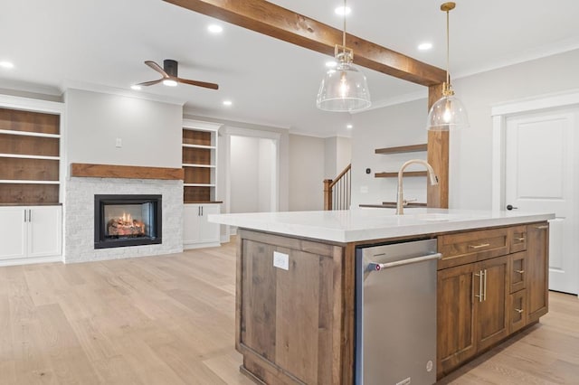 kitchen featuring built in shelves, hanging light fixtures, a stone fireplace, light hardwood / wood-style flooring, and a center island with sink