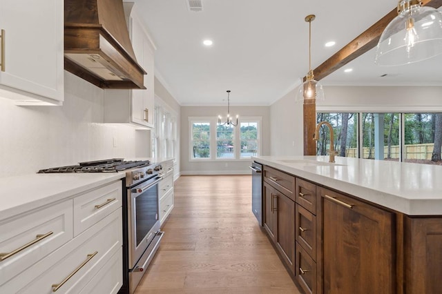 kitchen with white cabinets, wall chimney range hood, sink, decorative light fixtures, and stainless steel appliances